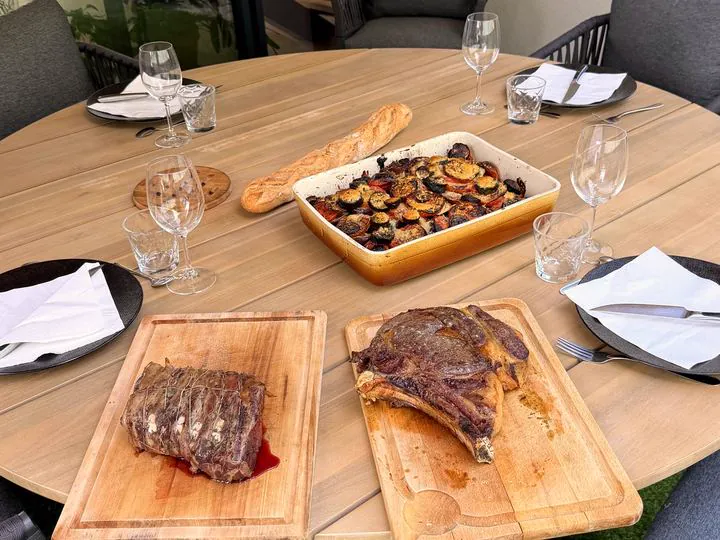 La grande table dressée dehors : viandes tranchées, légumes et pain